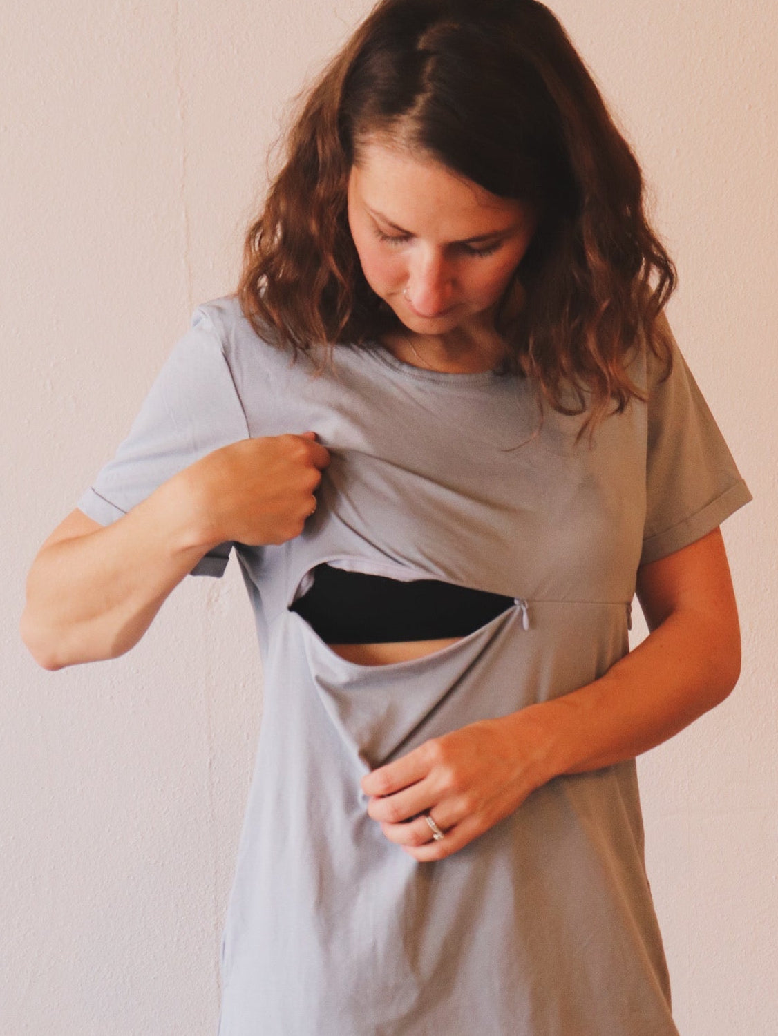 Woman wearing a light gray dress with a cutout design, standing against a plain background.